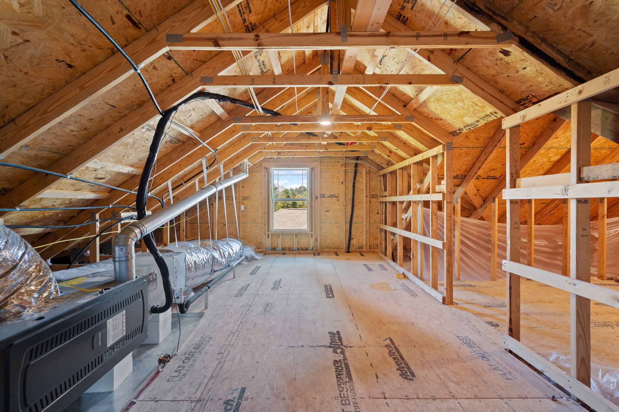 Unfinished attic with exposed roof framing, HVAC equipment, and a window at the far end.