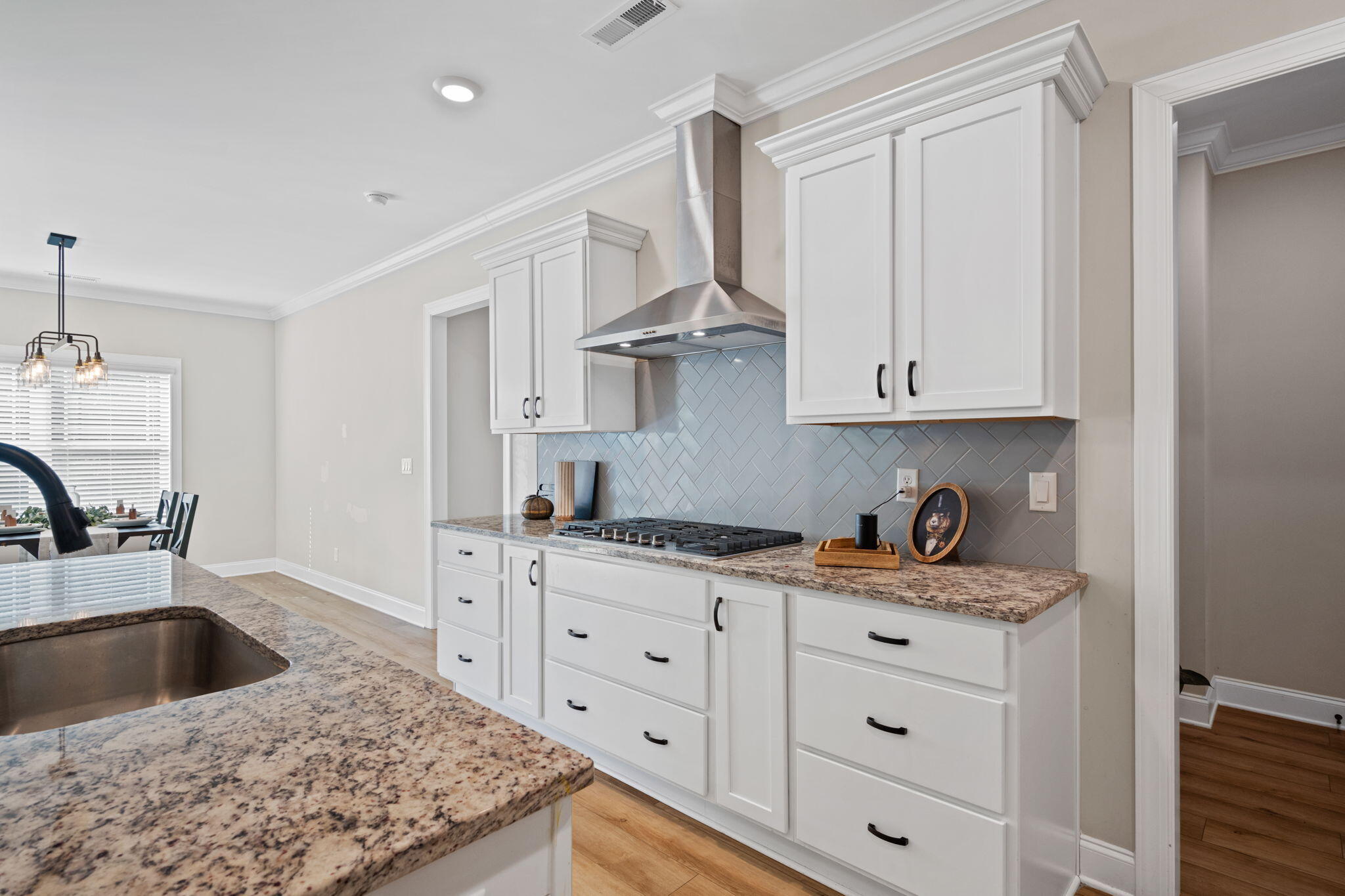 Kitchen with white shaker cabinets, gray diagonal tile backsplash, stainless range hood, and granite counters.