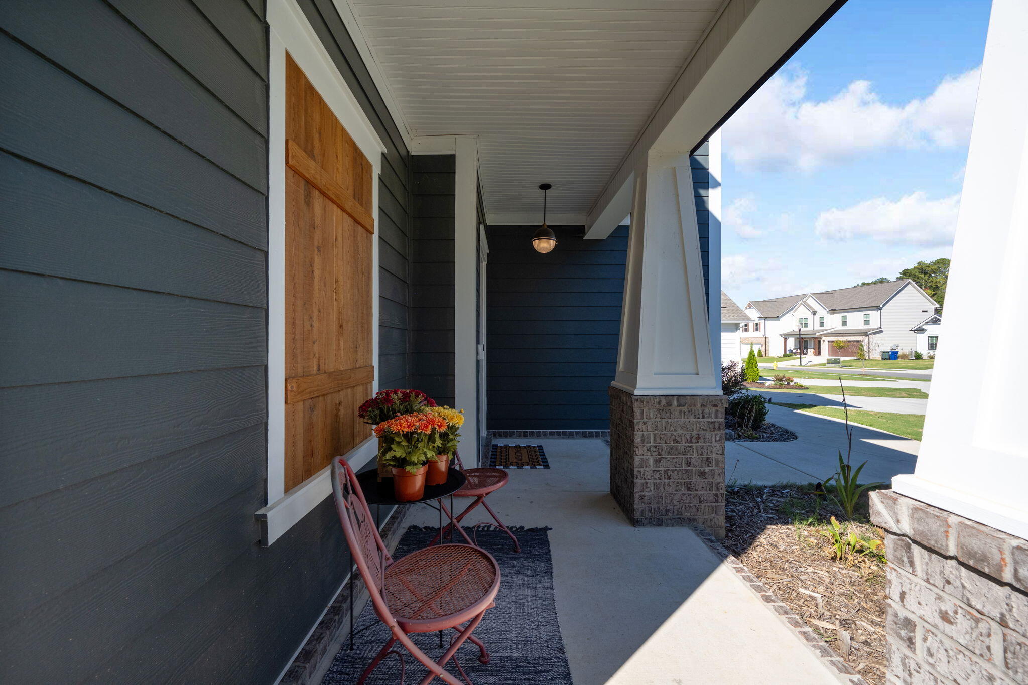 Covered front porch with a wood door, potted flowers, and seating beside the sunny neighborhood street.