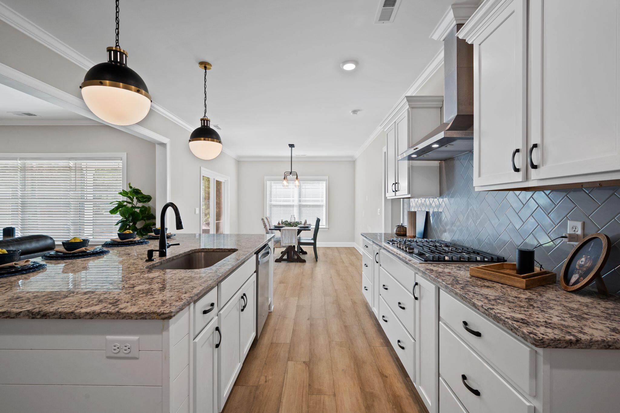 Bright kitchen with granite island, white cabinets, gray tile backsplash, and dining area beyond.