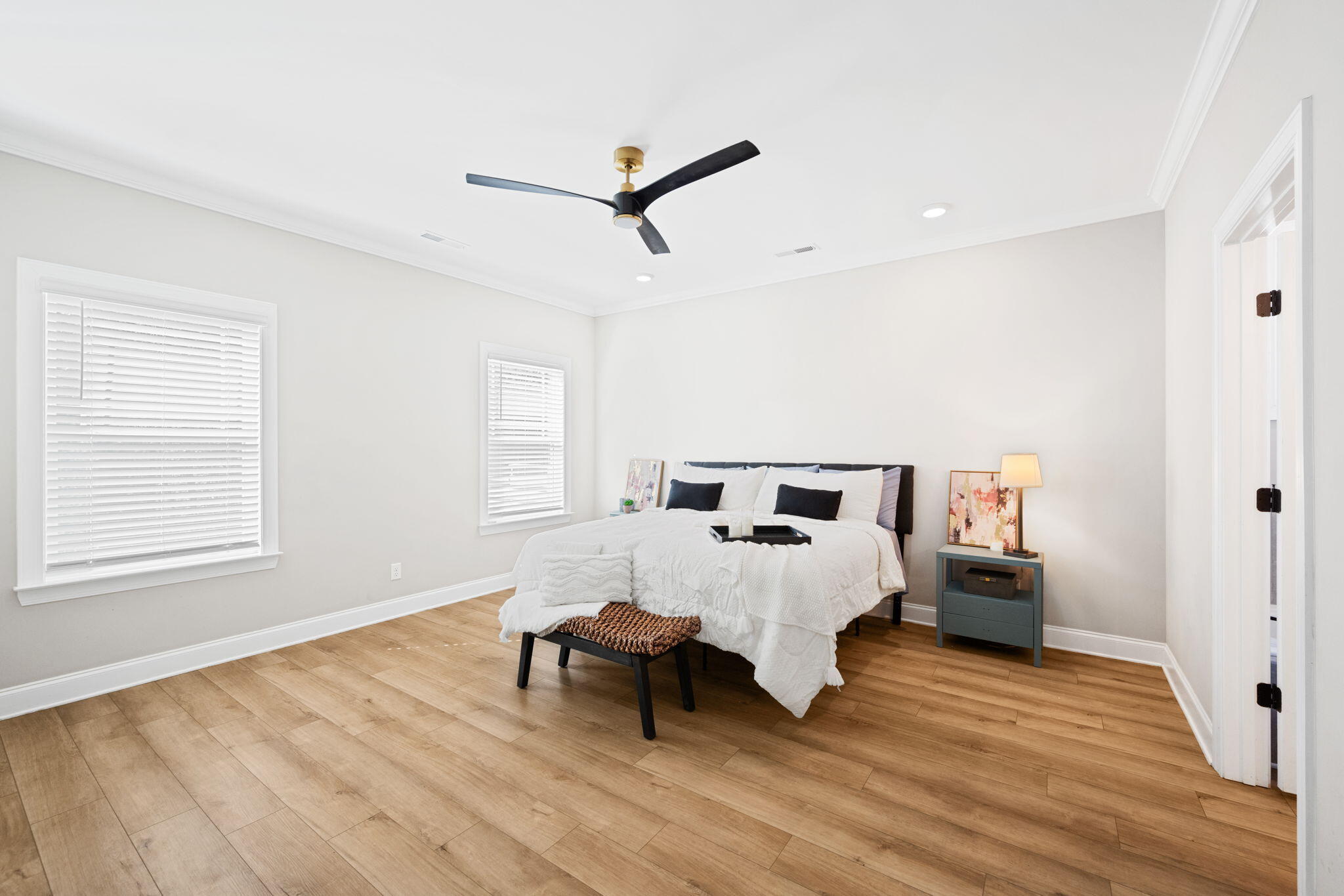 Furnished bedroom with a white bed, black ceiling fan, and warm wood-look flooring.