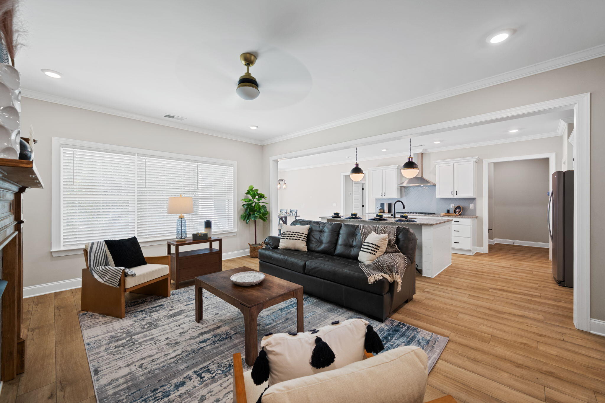 Open-plan living room with a black leather sofa beside a bright white kitchen.