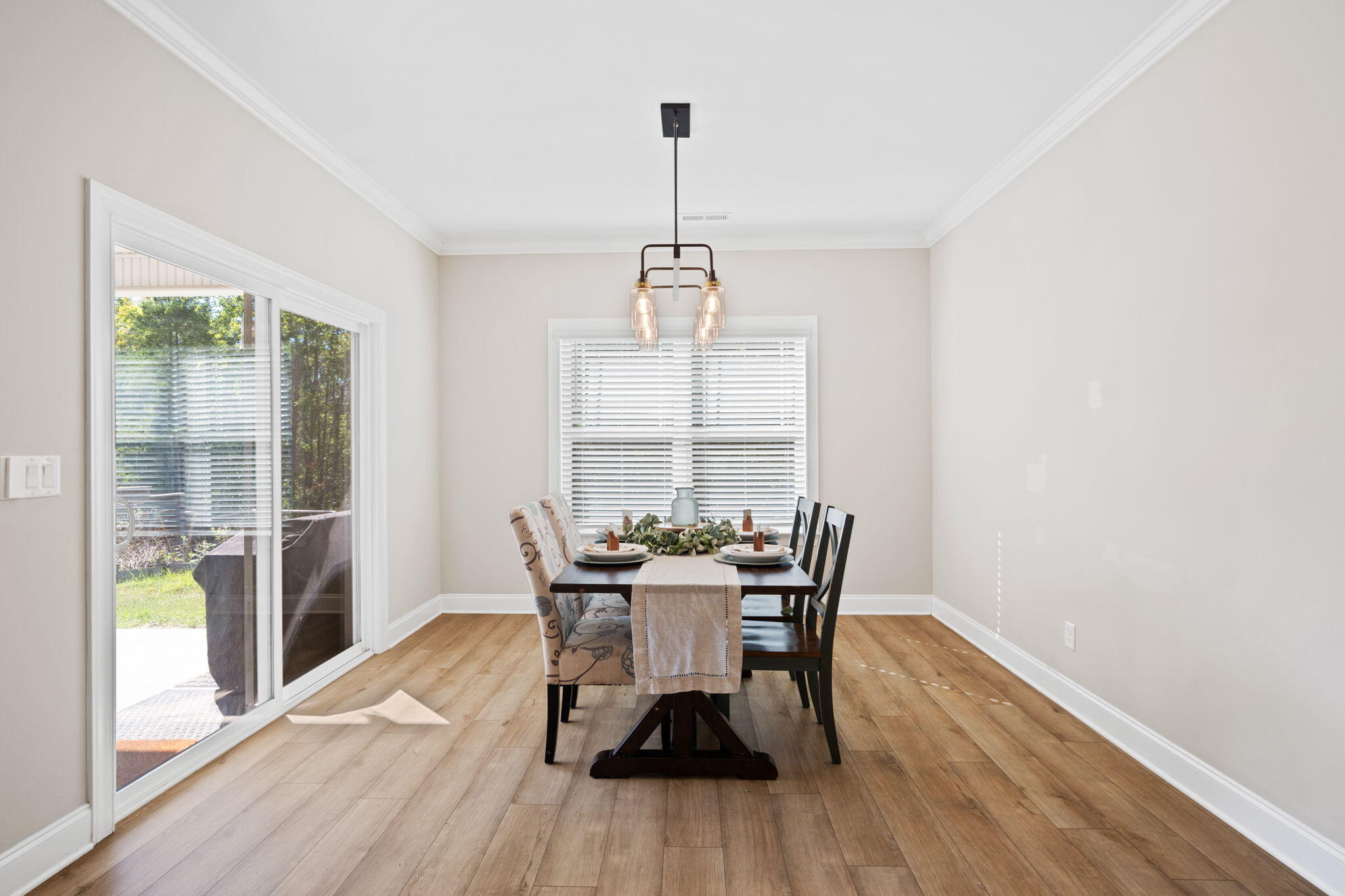 Dining room with a set table, pendant light, wood-look flooring, and sliding glass door to the patio.