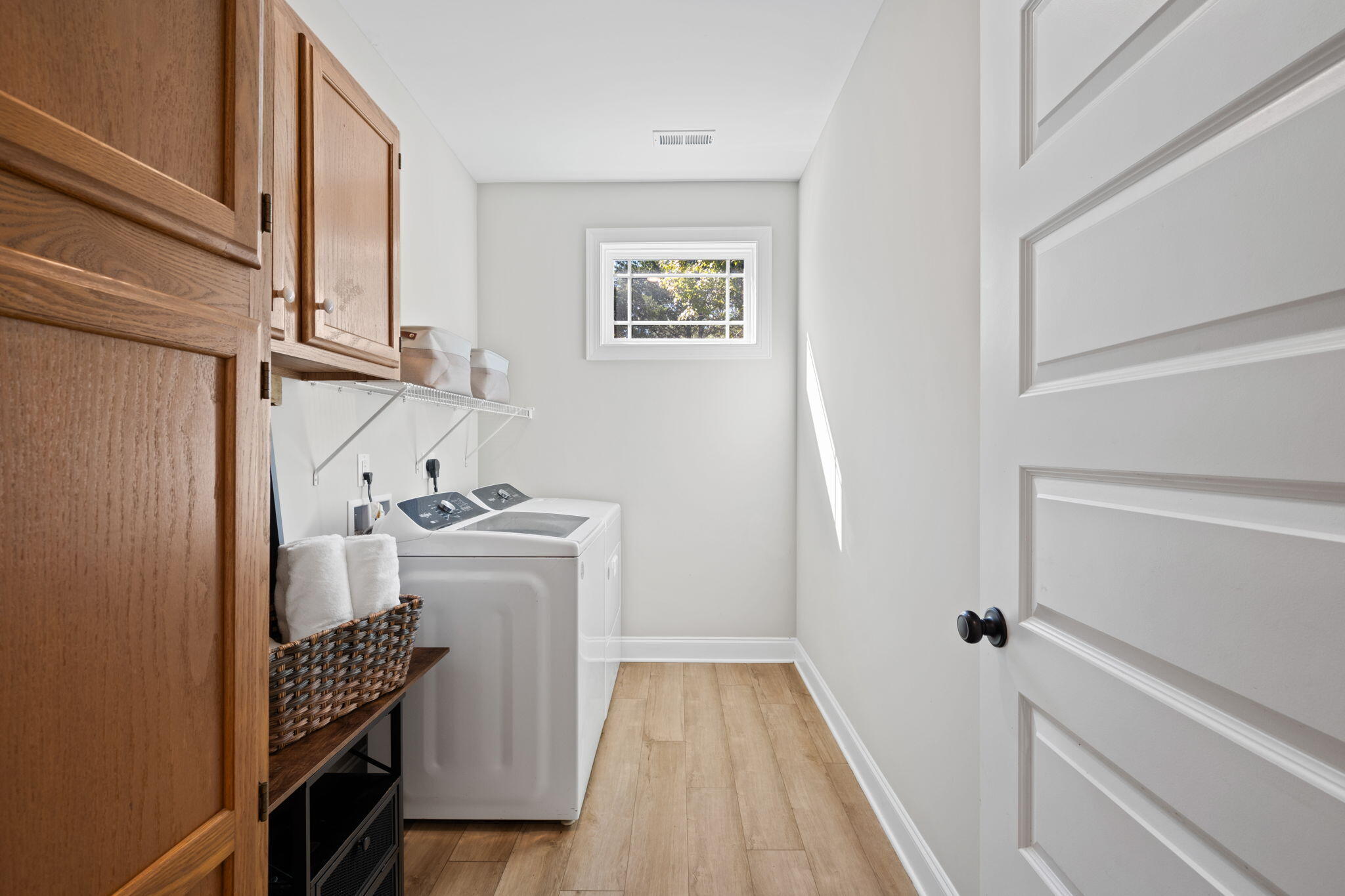 Laundry room with a top-loading washer, wood cabinets, and a basket of towels.