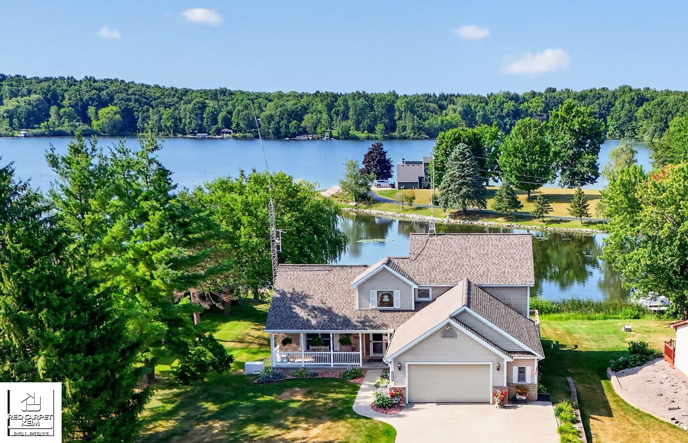Waterfront home with an attached garage, broad lawn, and wooded lake views.