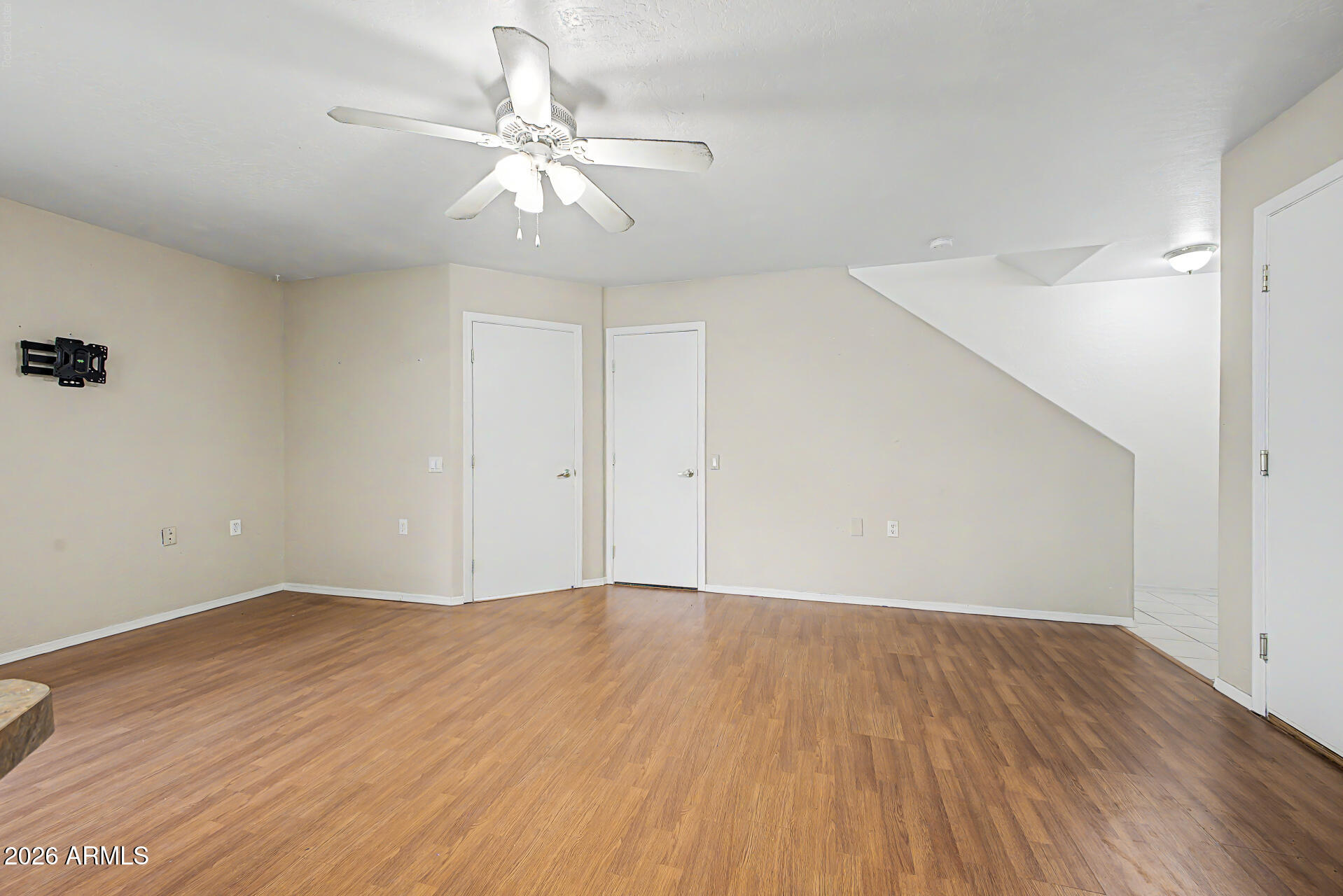 Vacant room with wood-look floors, ceiling fan, TV mount, and sloped stairway ceiling.