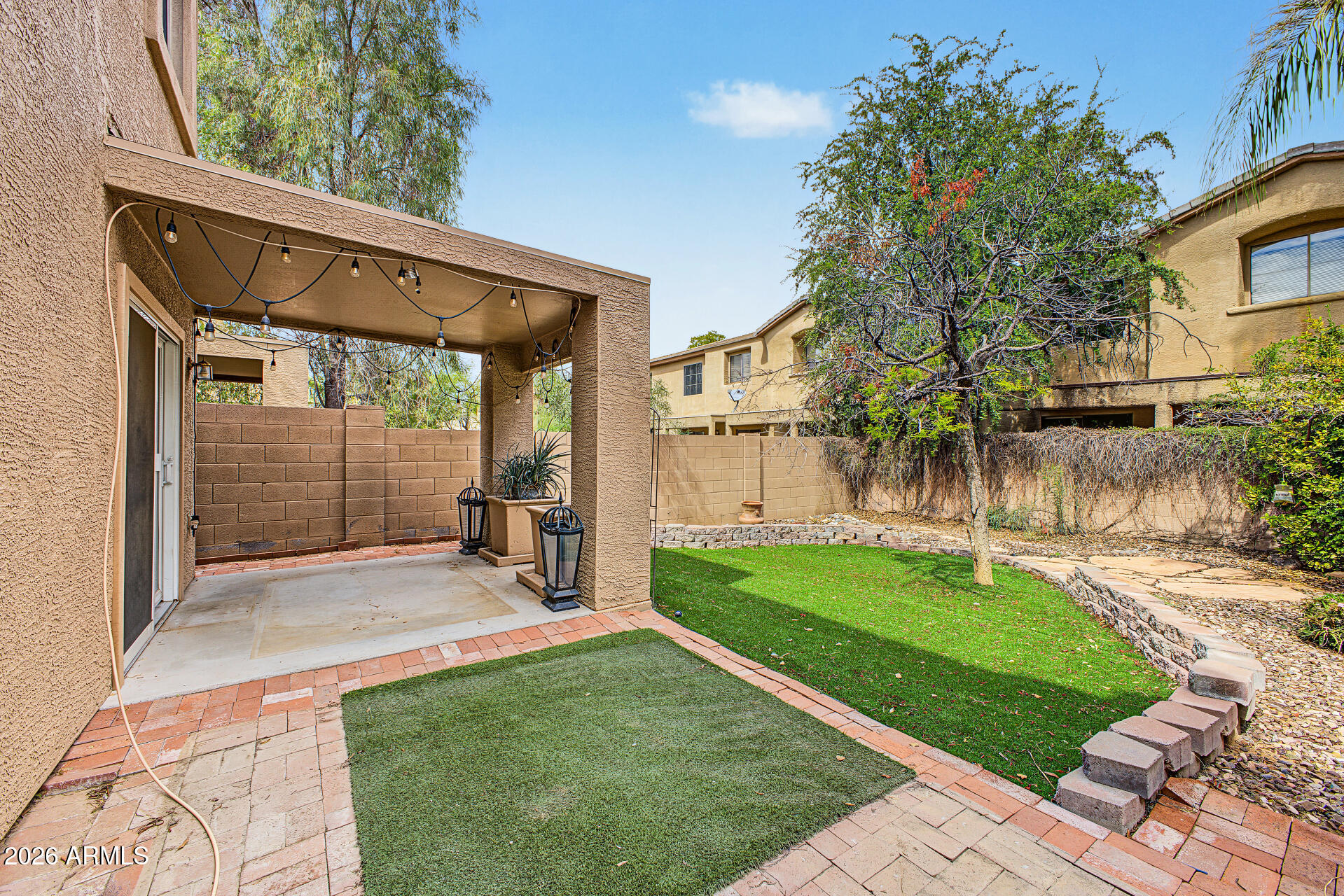 Backyard with a covered patio strung with lights beside a green lawn and mature trees.