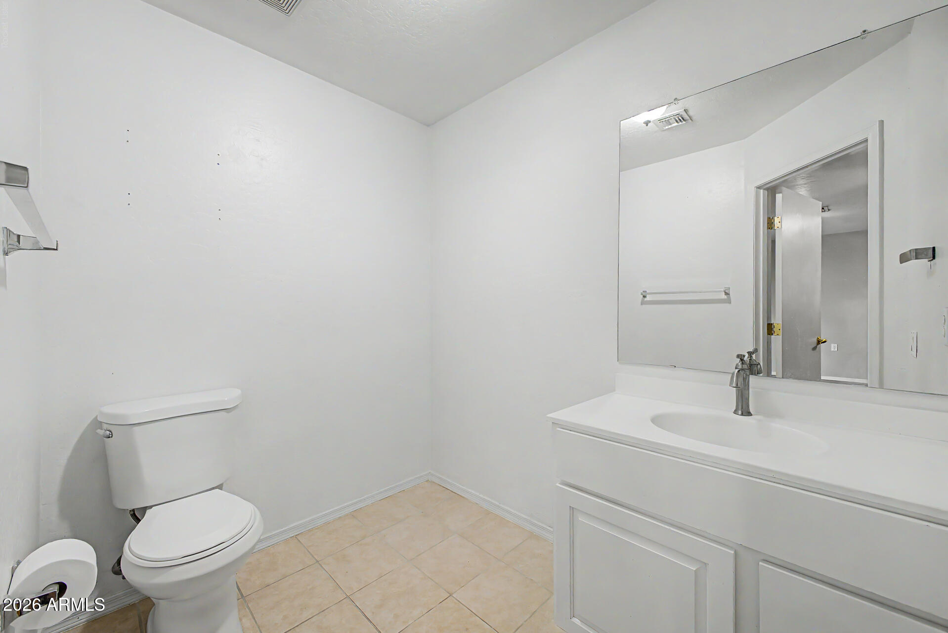 Empty bathroom with white toilet and vanity, large mirror, and beige tile floor.