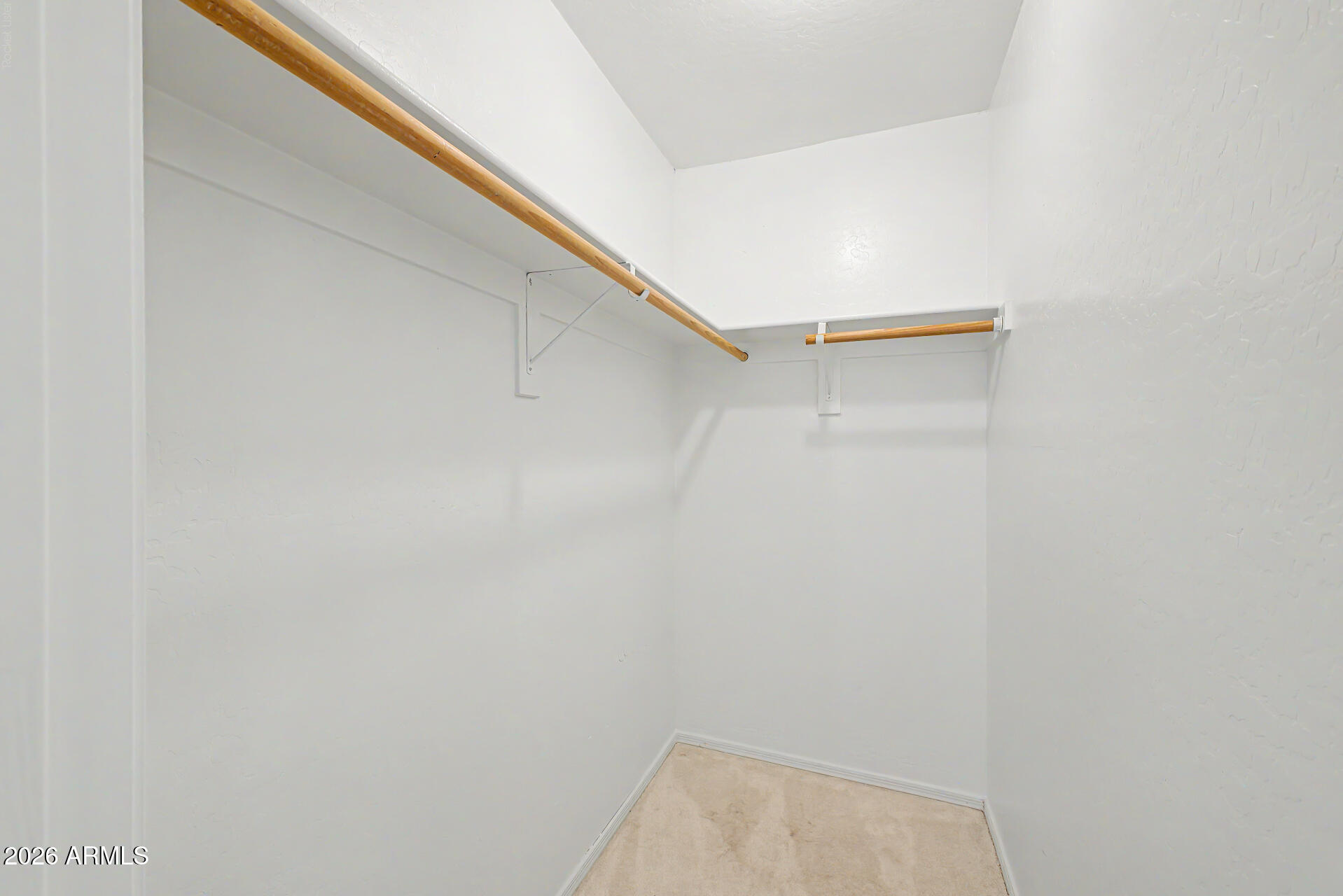 Empty walk-in closet with wooden hanging rods and beige carpet.