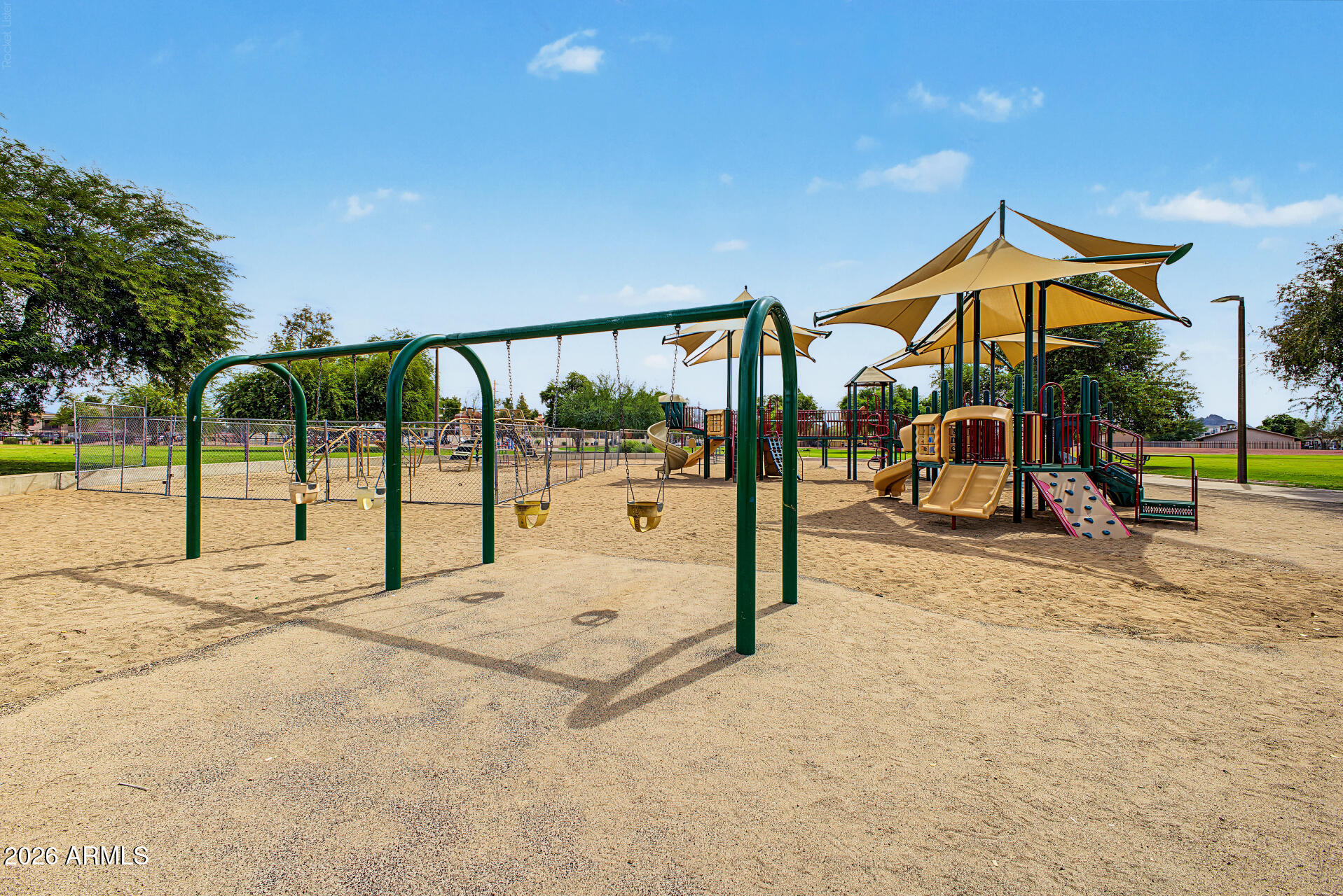 Community playground with swings and climbing structures under tan shade sails.