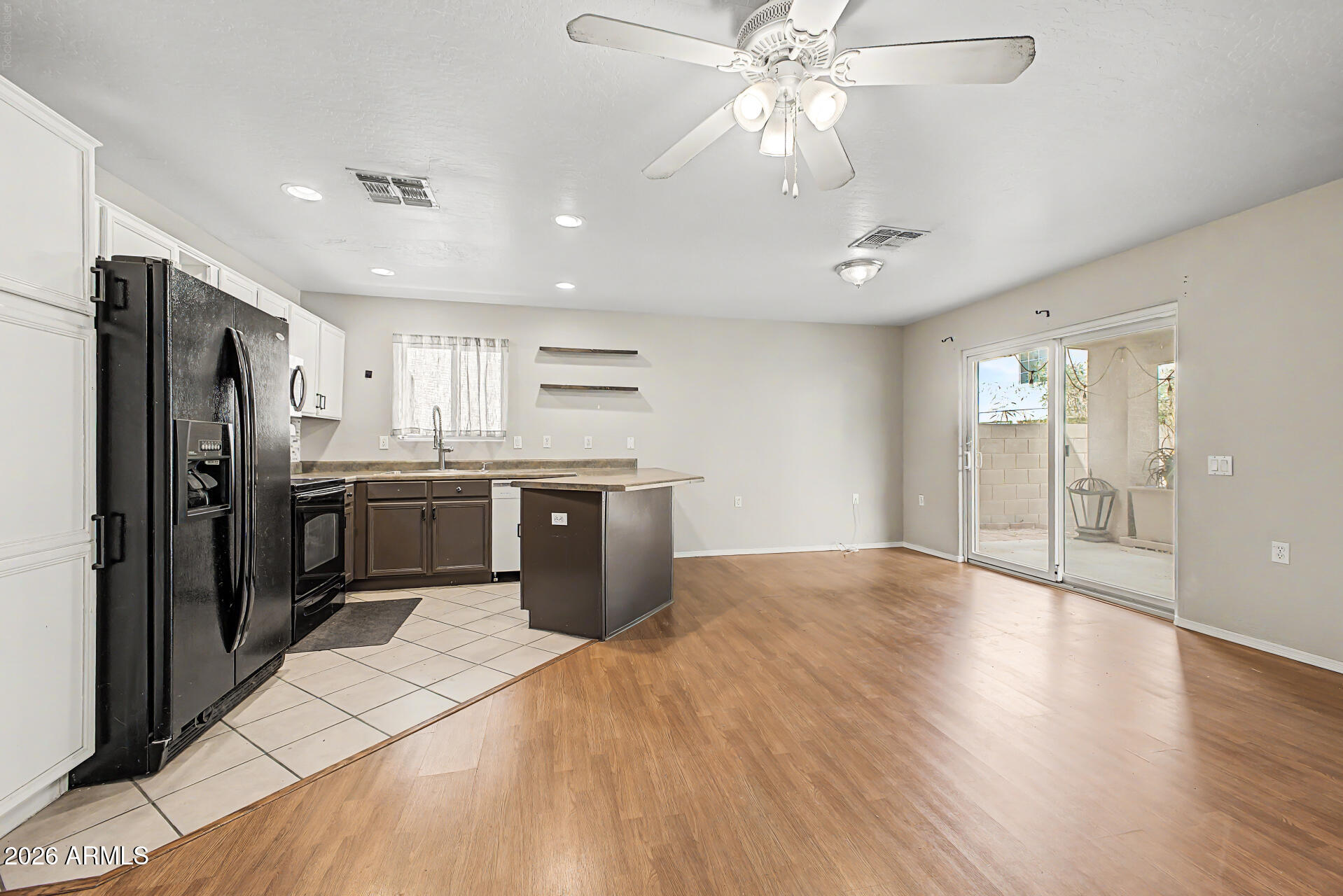 Kitchen and open dining area with dark cabinets, black appliances, wood flooring, and sliding glass patio doors.