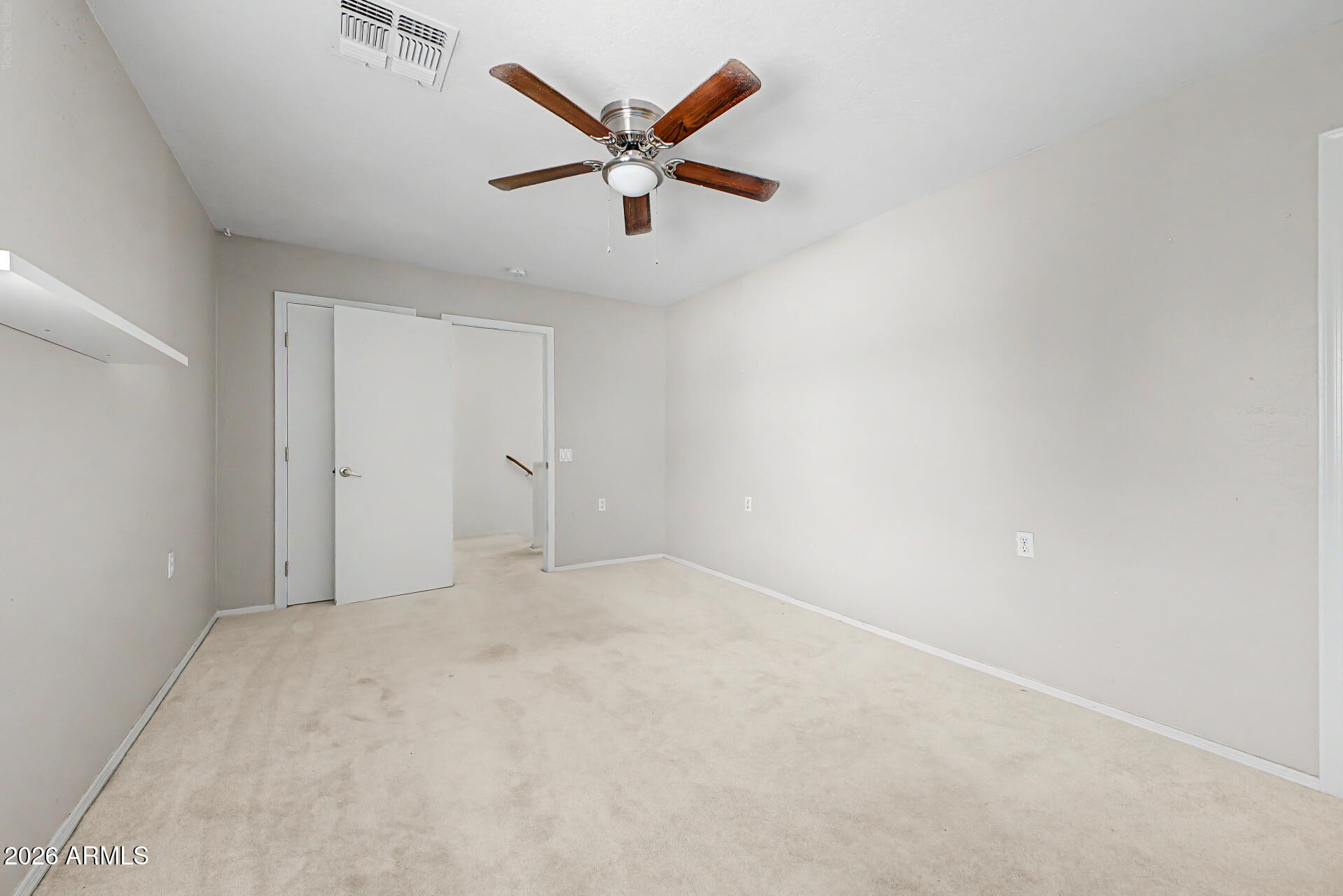 Empty carpeted room with a wooden-blade ceiling fan and open doors to an adjoining area.