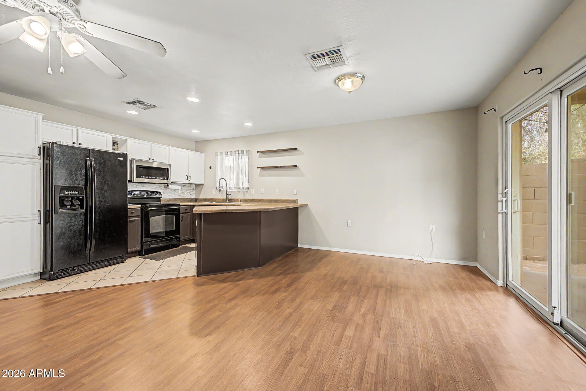 Kitchen with white cabinets, dark appliances, and a peninsula opening to an empty wood-floored room.