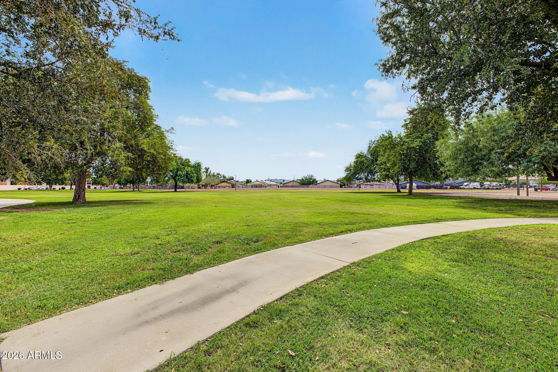 Neighborhood park with a broad lawn, mature shade trees, and a curving concrete walkway.