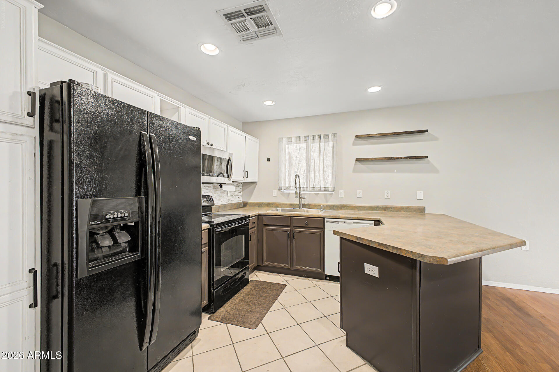 Kitchen with a large peninsula, black appliances, and a sink beneath a curtained window.