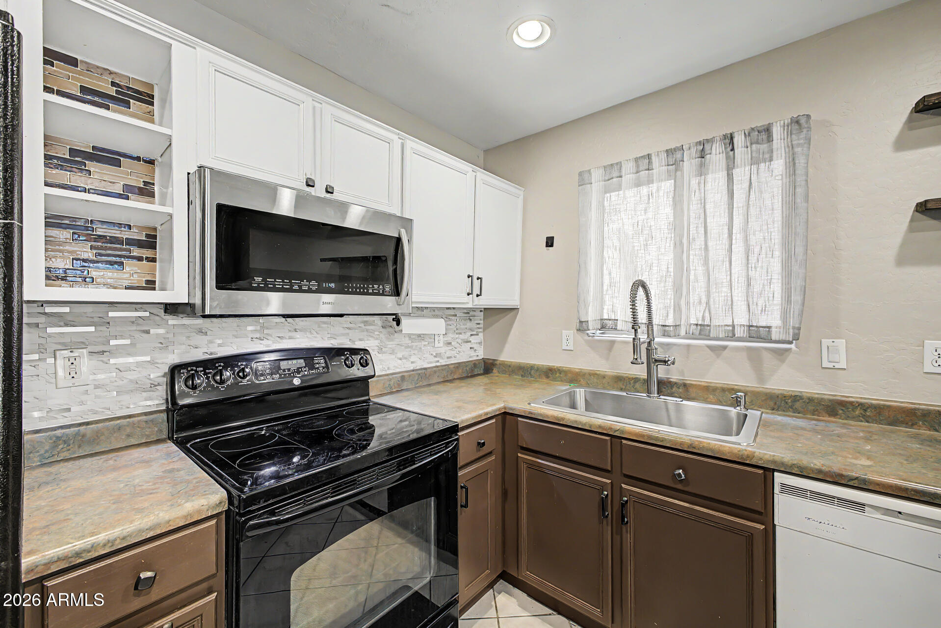 Kitchen with patterned tile backsplash, black range, and stainless sink beneath a curtained window.