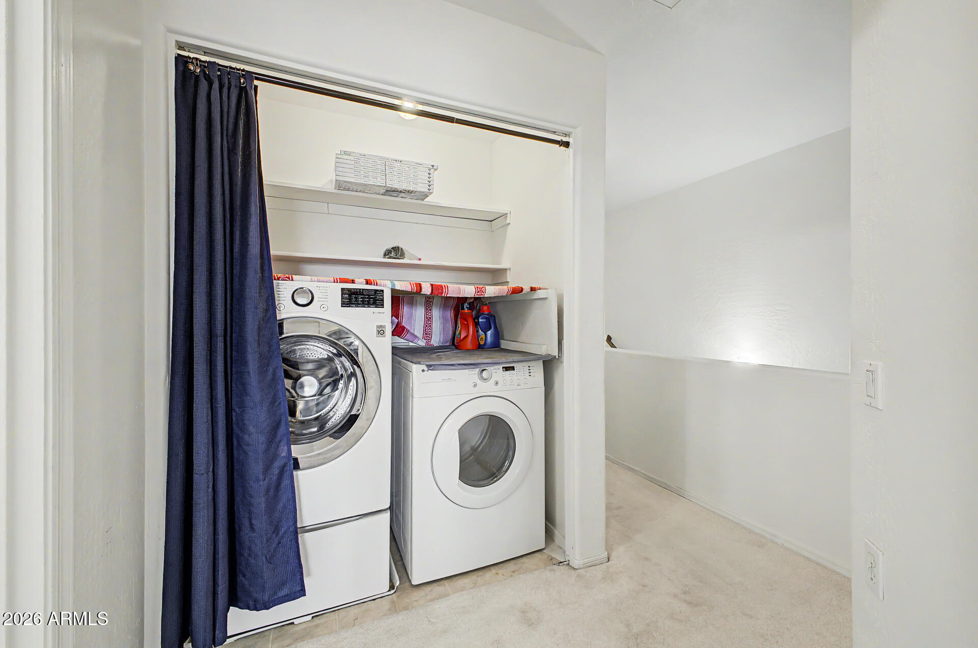 Laundry closet with side-by-side front-loading washer and dryer partly concealed by a dark blue curtain.