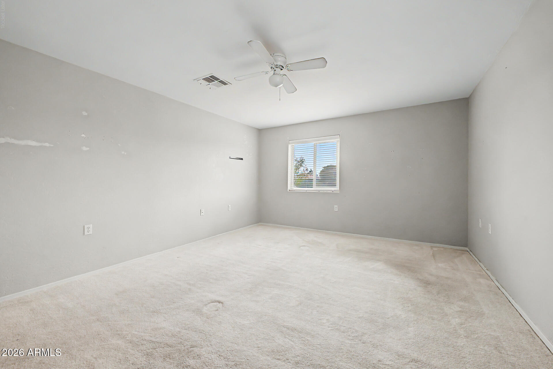 Empty carpeted room with gray walls, a ceiling fan, and a window with blinds.