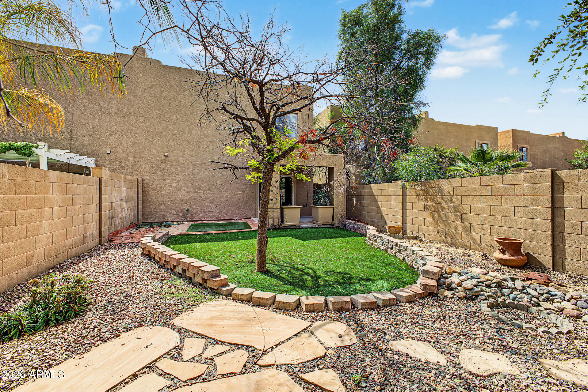 Enclosed backyard with a central lawn, gravel landscaping, stone pavers, and block walls.