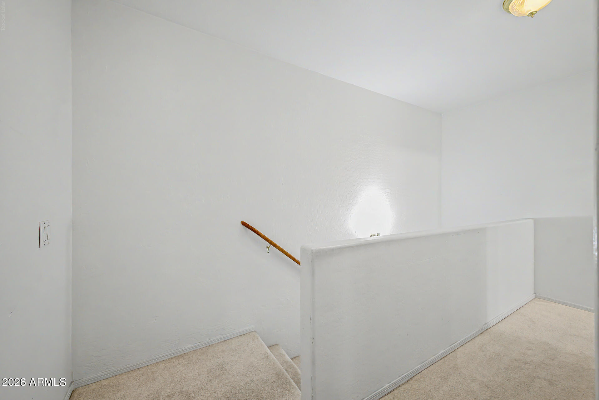 Carpeted staircase with a wooden handrail and white half-wall.