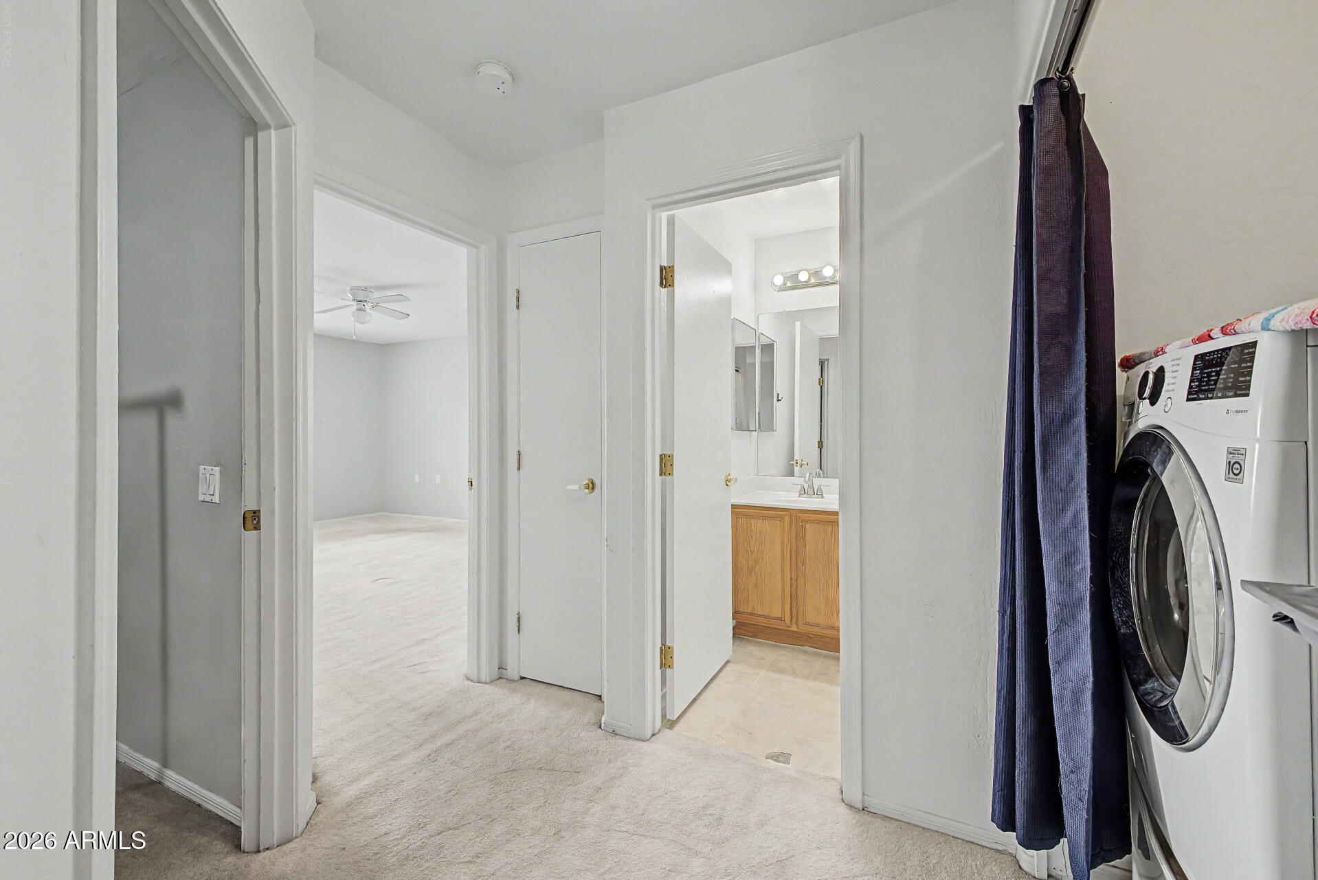 Hallway with a front-loading washer, open bathroom, and empty carpeted room.
