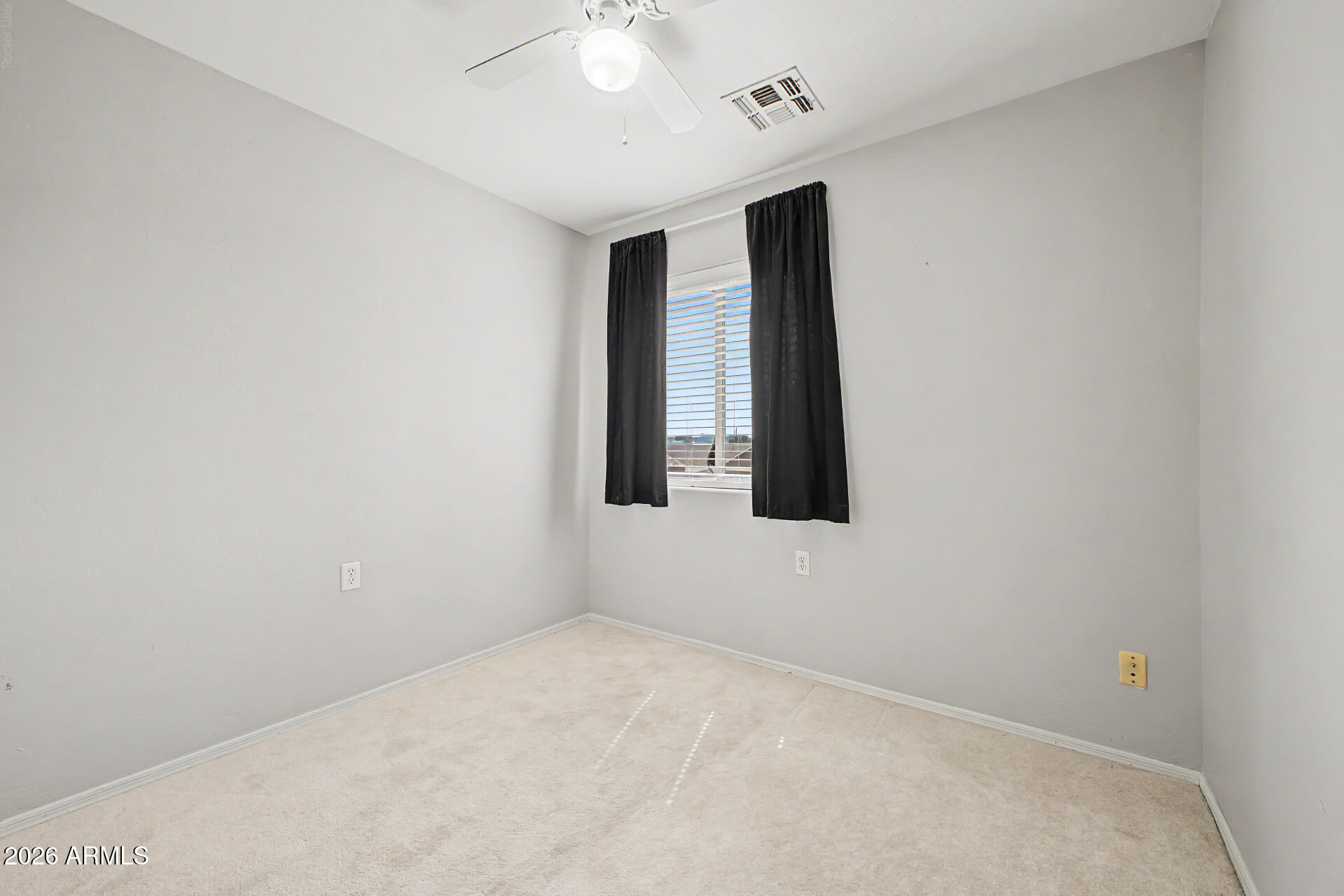 Empty bedroom with light carpet, black curtains, window blinds, and a ceiling fan.