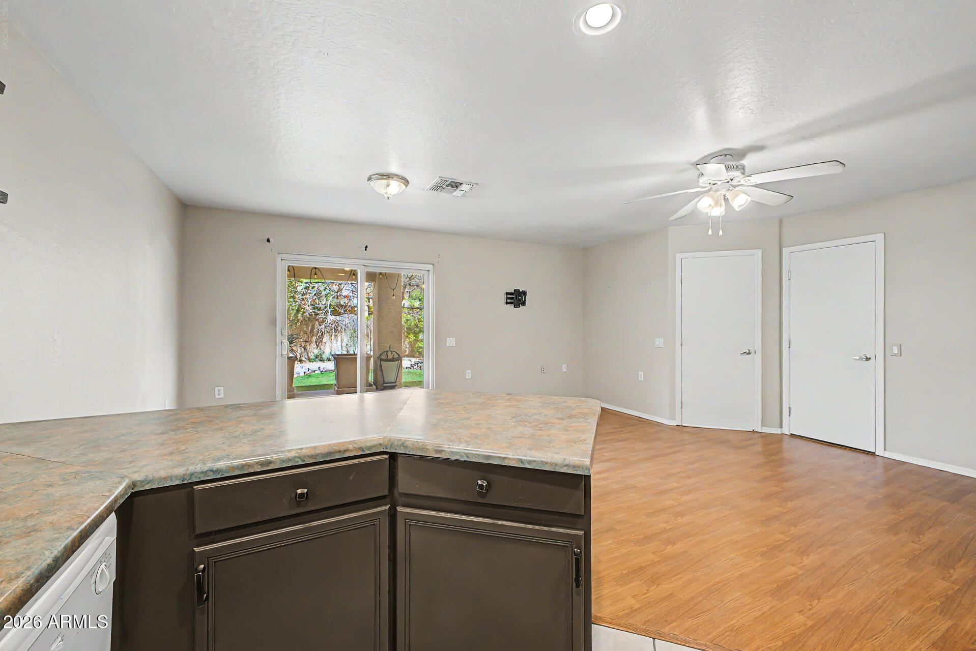 Kitchen island with dark cabinets and mottled countertop overlooking an unfurnished room with sliding glass doors.
