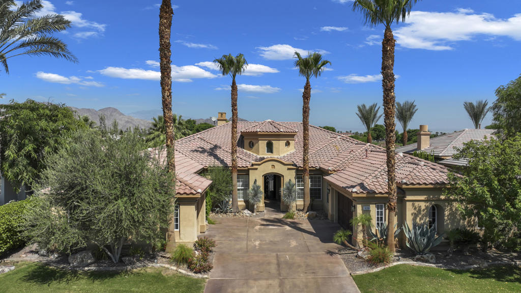 Mediterranean-style home with a tiled roof, palm trees, and a broad driveway.
