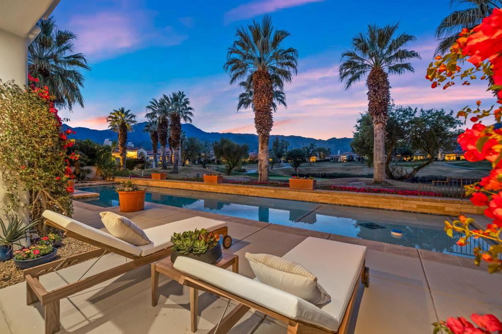 Backyard pool and patio with lounge chairs, palm trees, and mountains at dusk.