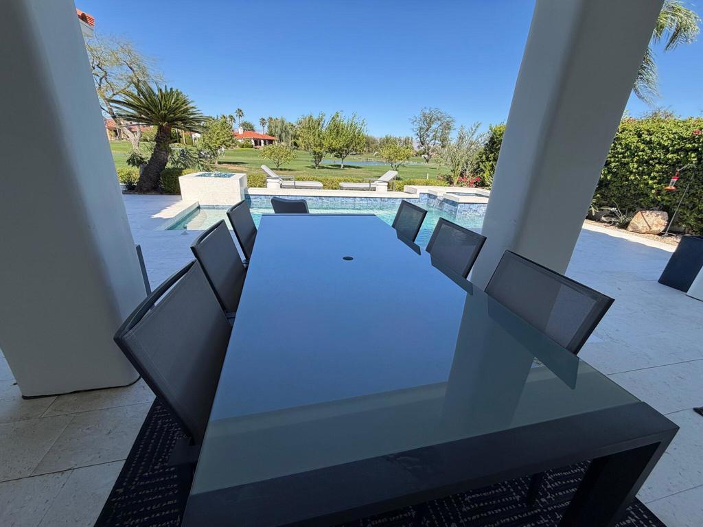Covered patio dining area overlooking a swimming pool, lawn, and pond.