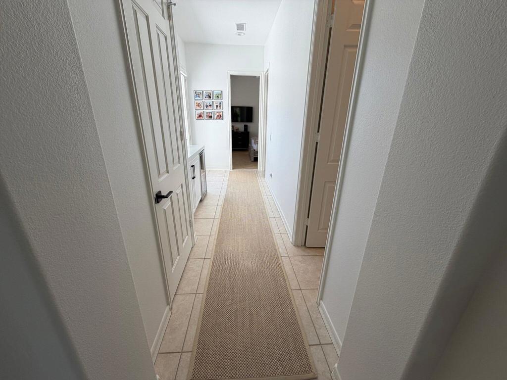 Bright tiled hallway with a long woven runner, white paneled doors, and built-in cabinetry.