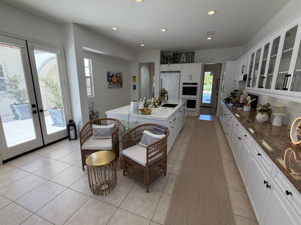 Bright white kitchen with a long island, glass-front cabinets, and a small seating area.