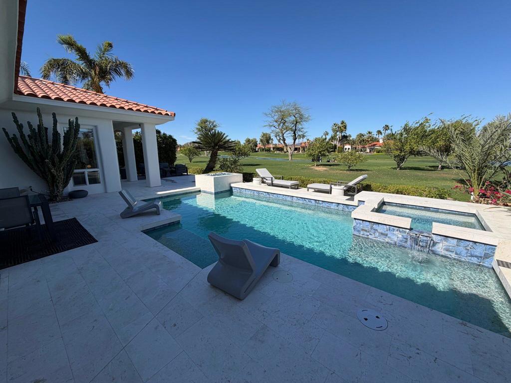 Backyard pool beside a covered patio, with lounge chairs and a golf course beyond.