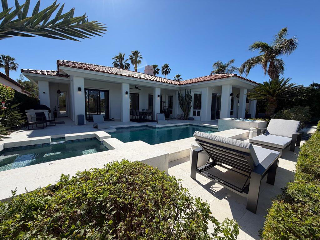 Single-story home with a swimming pool, pale stone patio, and outdoor loungers.