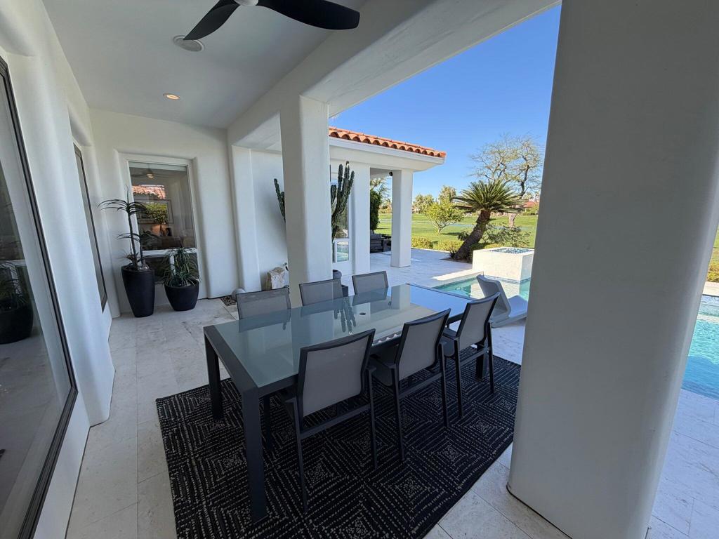 Covered patio with a glass dining table overlooking the pool and lawn.