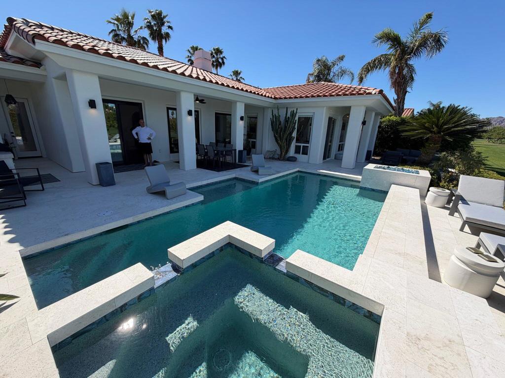 Modern white home with a red tile roof overlooking a turquoise pool and raised spa.