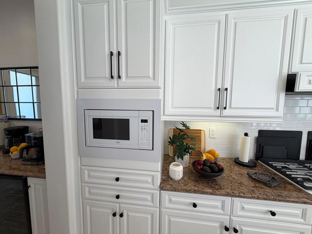 Kitchen with white paneled cabinets, a built-in microwave, granite counters, and a gas cooktop.