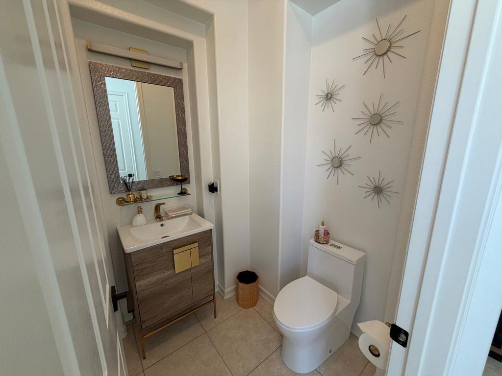 Powder room with a wood vanity, white toilet, and sunburst wall decor.