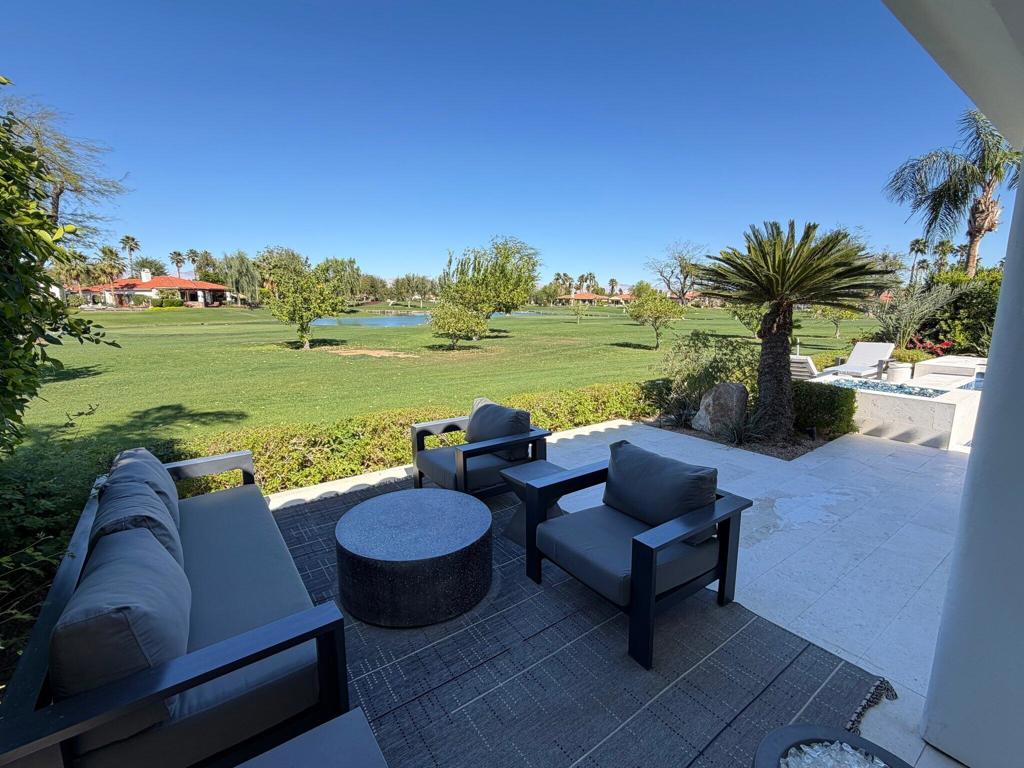 Furnished stone patio overlooking a golf course, with outdoor seating and a small pond.