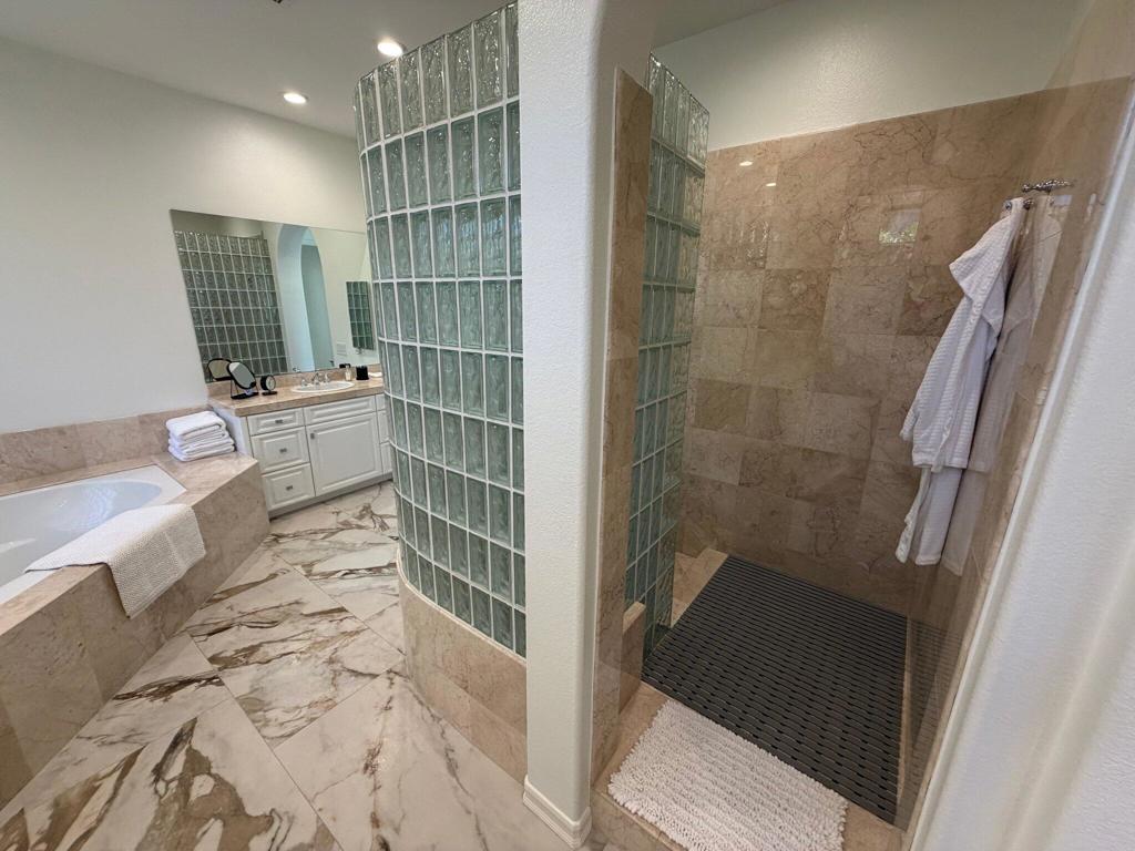 Bathroom with a glass-block shower, marble tile, soaking tub, and double vanity.