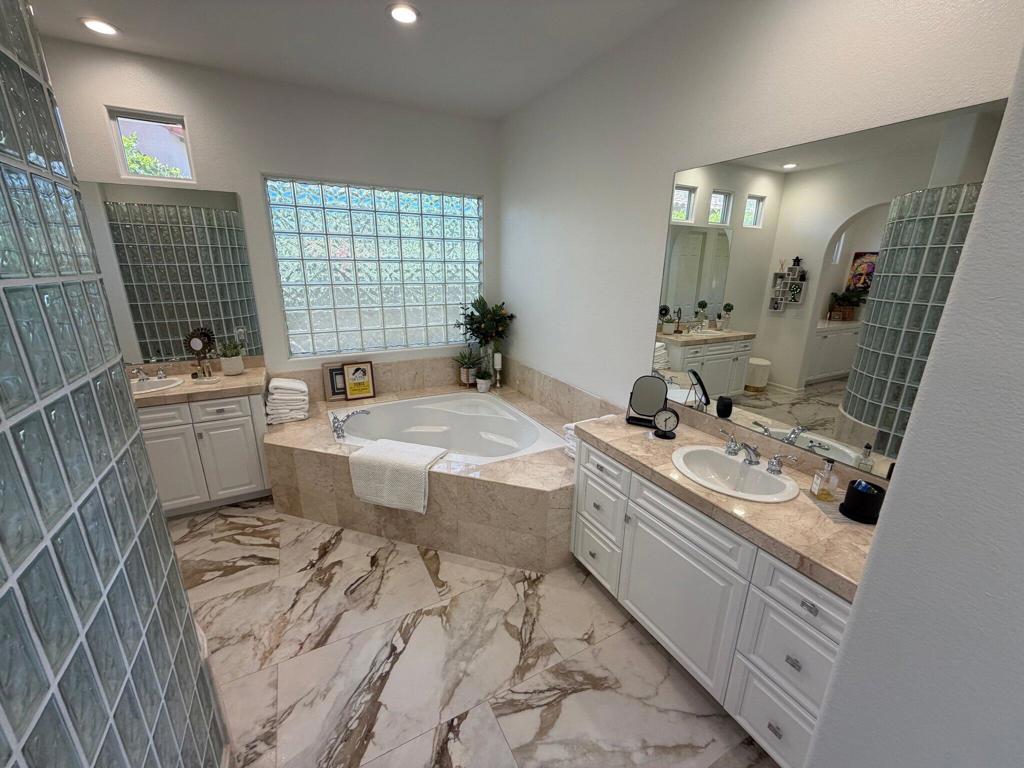 Primary bathroom with a corner soaking tub, glass-block walls, and a double-sink vanity.