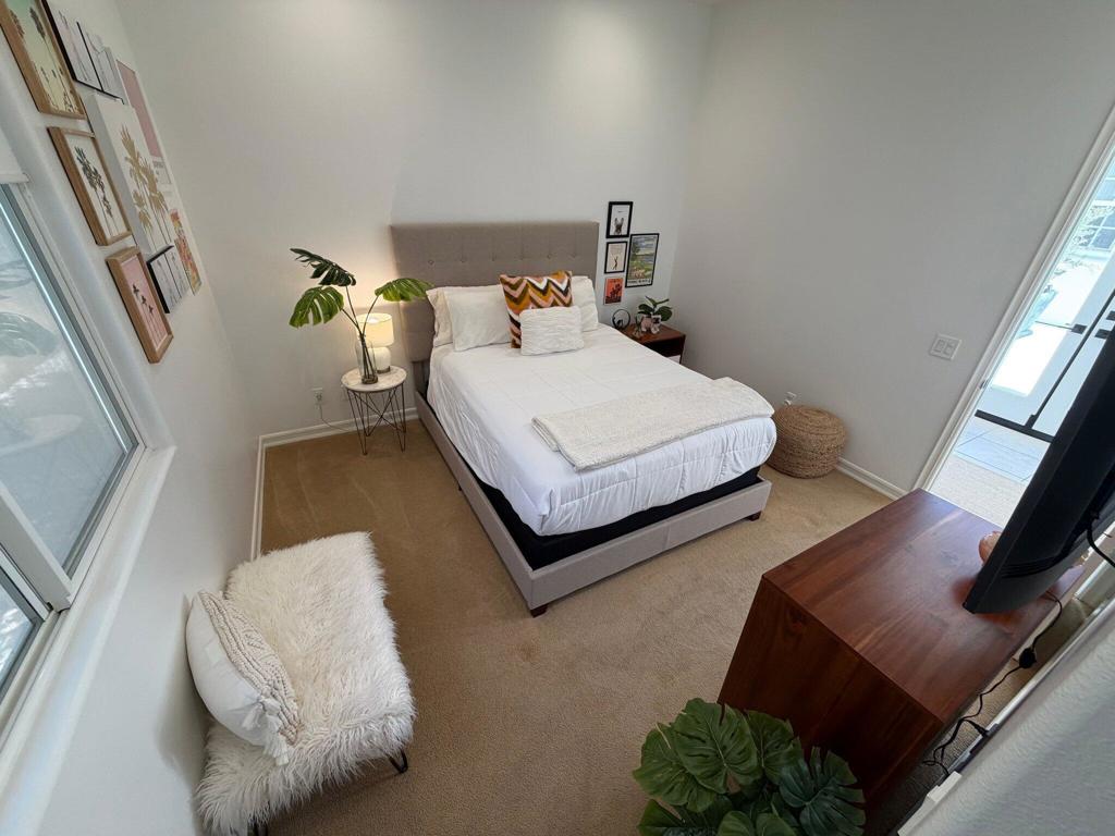 Bedroom with a neatly made bed, wall art, plants, and a glass door to the patio.
