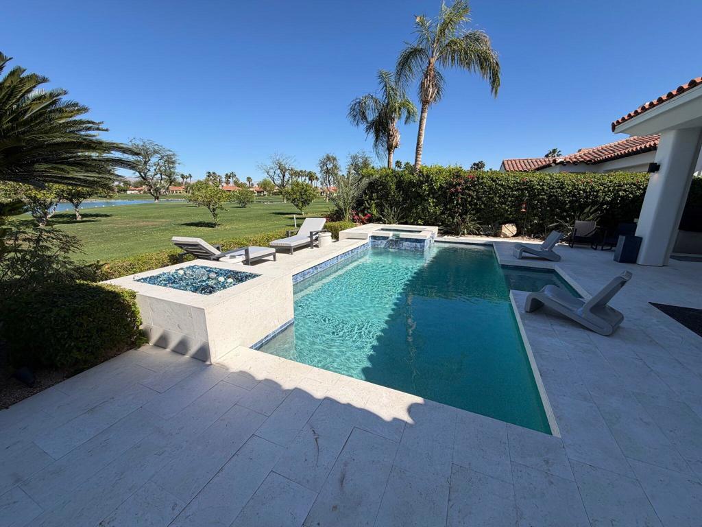 Backyard pool and raised spa overlook a green golf course, with palms and patio loungers.