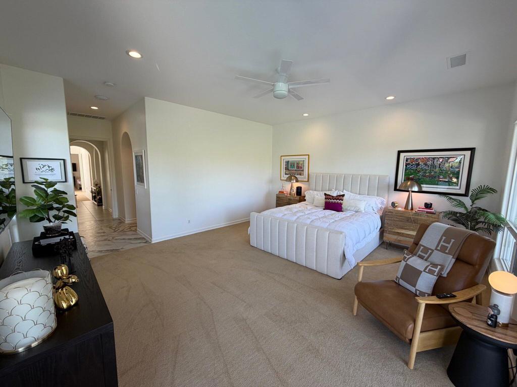 Staged bedroom with a white bed, tan carpet, and leather accent chair.