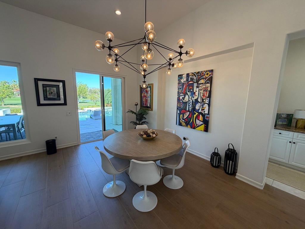 Dining room with a round table beneath a sculptural chandelier, opening to a pool patio.