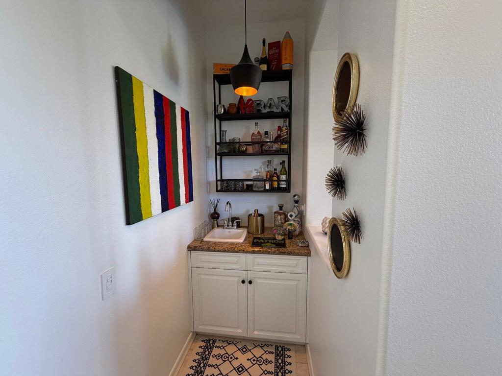 Wet bar with a small sink, stocked shelves, and colorful striped wall art.