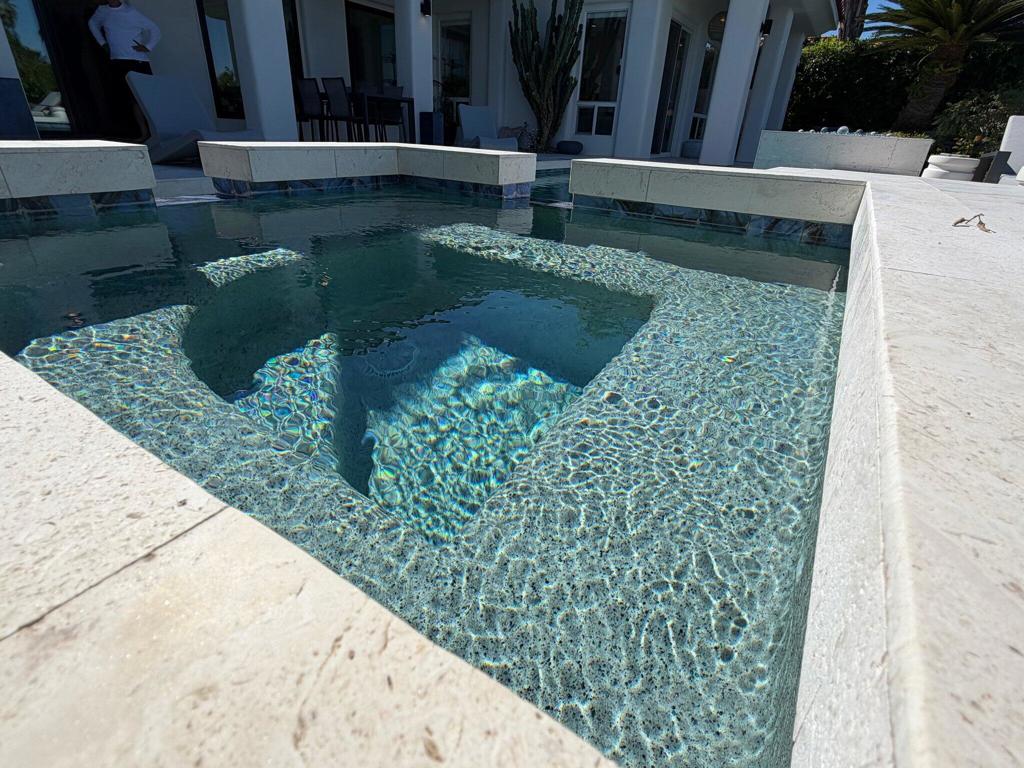 Backyard pool with a shallow sun shelf and stone coping beside the house.