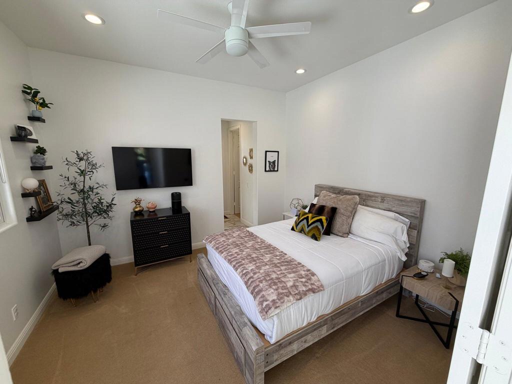 Bedroom with a gray wood bed, wall-mounted television, and ceiling fan.