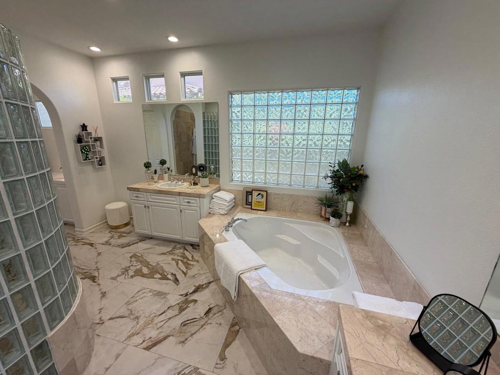 Bathroom with a corner soaking tub, double vanity, glass-block window, and marble floors.