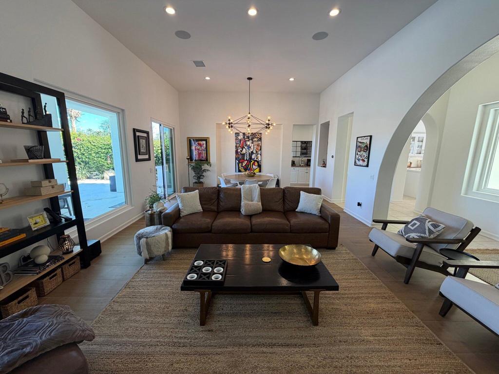 Living room with a brown sectional, large rug, colorful artwork, and an arched opening to the kitchen.